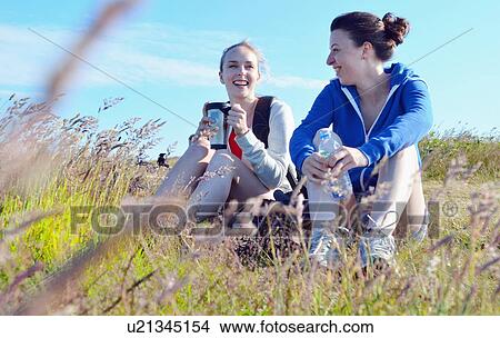 Two young women sitting on grass, drinking and talking View Large Photo Image Picture - Two young women sitting on grass, drinking and talking. Fotosearch