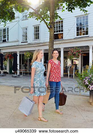 Stock Photo - Two young women strolling along street carrying shopping bags. Fotosearch