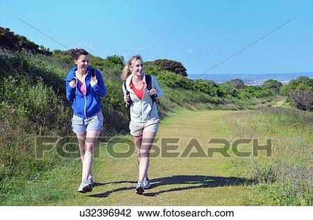 Stock Image - Two young women walking along coastal path. Fotosearch
