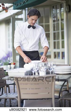Waiter folding napkins in patio restaurant View Large Photo Image Stock Image - Waiter folding napkins in patio restaurant. Fotosearch