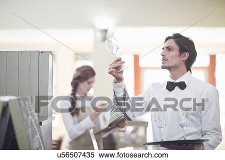 Stock Photography - Waiter holding up and checking wine glass in restaurant. Fotosearch
