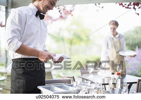 Waiter polishing cutlery with napkin in patio restaurant View Large Photo Image Stock Photography - Waiter polishing cutlery with napkin in patio restaurant. Fotosearch