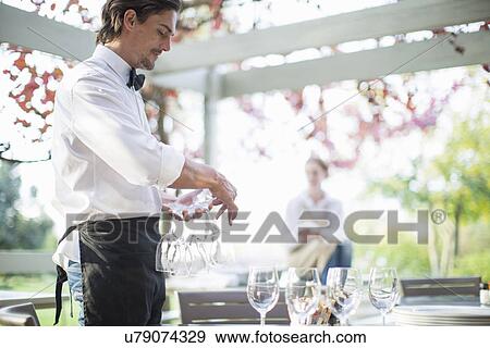 Waiter preparing wine glasses on table in patio restaurant View Large Photo Image Stock Photo - Waiter preparing wine glasses on table in patio restaurant. Fotosearch