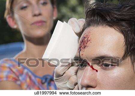Picture - Woman cleaning young man with bleeding forehead. Fotosearch