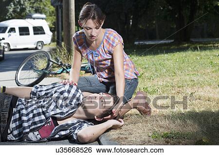 Stock Photograph - Woman helping injured man lying on roadside. Fotosearch