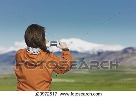 Stock Photo - Woman taking picture with smartphone of Snaefellsnes glacier, Iceland. Fotosearch