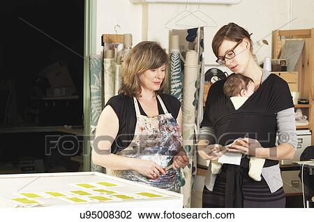 Stock Image - Women discussing design in hand-printing textile workshop. Fotosearch
