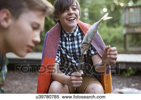 Stock Photography - Young boy holding stick with fish on ready to barbecue. Fotosearch
