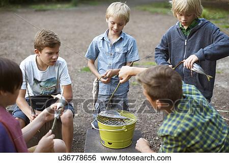 Stock Photograph - Young boys cooking fish over barbecue. Fotosearch