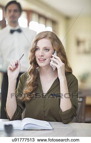 Stock Image - Young businesswoman chatting on smartphone in restaurant. Fotosearch
