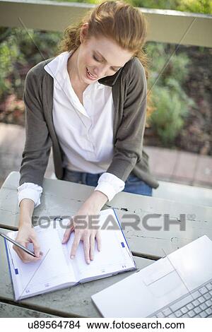 Young businesswoman writing in work diary at garden table View Large Photo Image Picture - Young businesswoman writing in work diary at garden table. Fotosearch