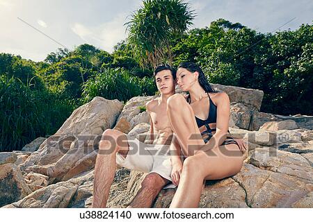 Stock Image - Young couple sitting together on rocks. Fotosearch