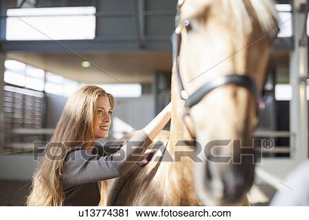 Young female stablehand grooming palomino horse View Large Photo Image Stock Image - Young female stablehand grooming palomino horse. Fotosearch