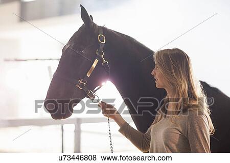 Stock Photo - Young female stablehand leading nervous horse. Fotosearch