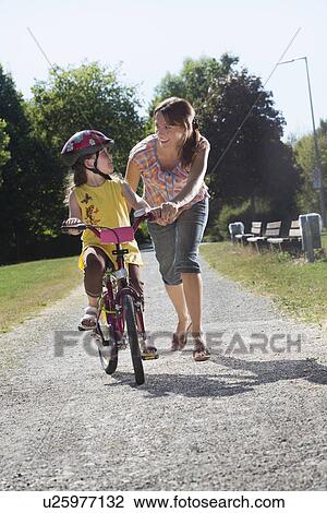 Stock Image - Young girl learning to ride bicycle with mother. Fotosearch