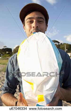 Picture - Young man blowing up beach ball on Bournemouth beach, Dorset, UK. Fotosearch