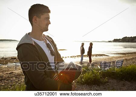 Stock Image - Young man holding blanket on Bournemouth beach, Dorset, UK. Fotosearch