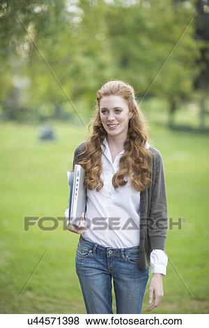 Young woman carrying laptop and walking in park View Large Photo Image Stock Photo - Young woman carrying laptop and walking in park. Fotosearch