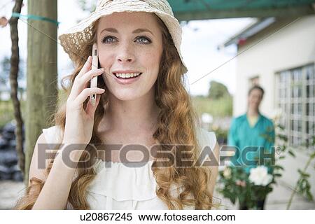 Stock Photography - Young woman chatting on smartphone in rose garden centre. Fotosearch