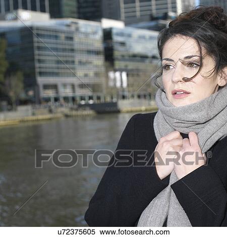 Stock Photography - Young woman holding onto wrapped scarf at city riverside. Fotosearch