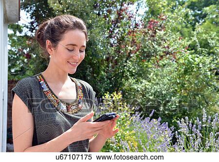 Young woman in garden reading text message on smartphone View Large Photo Image Stock Photography - Young woman in garden reading text message on smartphone. Fotosearch