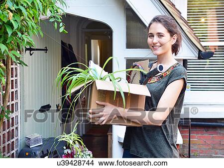 Picture - Young woman outside new house carrying cardboard box. Fotosearch