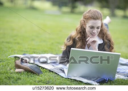 Young woman reclining on picnic blanket using laptop in park View Large Photo Image Stock Image - Young woman reclining on picnic blanket using laptop in park. Fotosearch