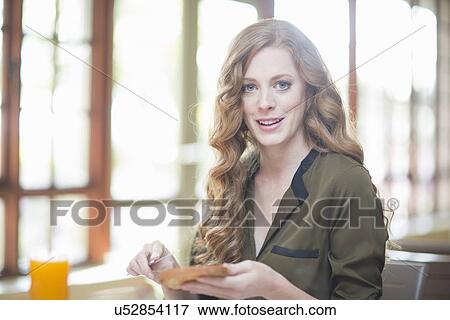 Stock Photo - Young woman sitting at restaurant table with slice of toast. Fotosearch