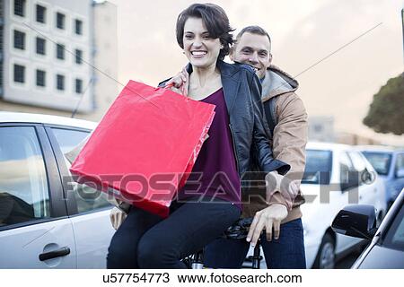 Young woman sitting on bicycle handlebar moving through city traffic jam View Large Photo Image Stock Image - Young woman sitting on bicycle handlebar moving through city traffic jam. Fotosearch