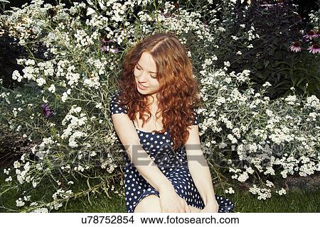 Picture - Young woman sitting on park grass looking sideways. Fotosearch