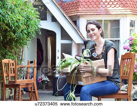 Stock Photography - Young woman sitting outside new house with cardboard box. Fotosearch