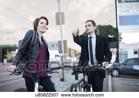 Stock Photo - Young woman taking directions from businessman whilst cycling in city. Fotosearch