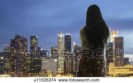 Picture - Young woman with suitcase looking at city skyline. Fotosearch