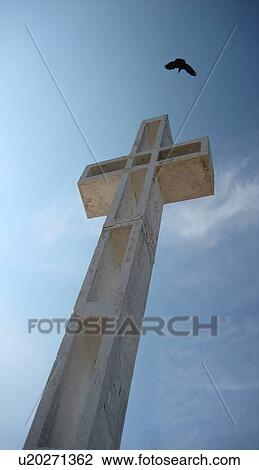 Stock Image - Bird flying by a cross . Fotosearch