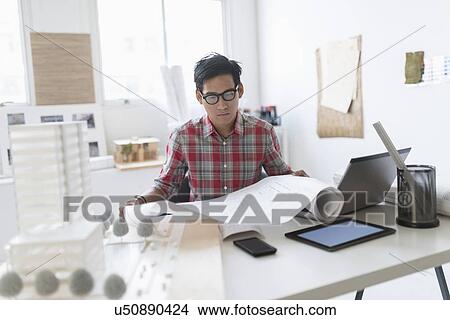 Picture - Architect looking at blueprints in office. Fotosearch