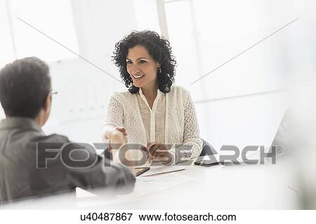 Business people shaking hands at desk in office View Large Photo Image Stock Photo - Business people shaking hands at desk in office. Fotosearch