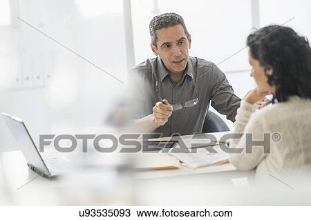 Stock Image - Business people talking at desk in office. Fotosearch