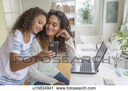 Stock Image - Daughter (8-9) and mother looking at smart phone. Fotosearch