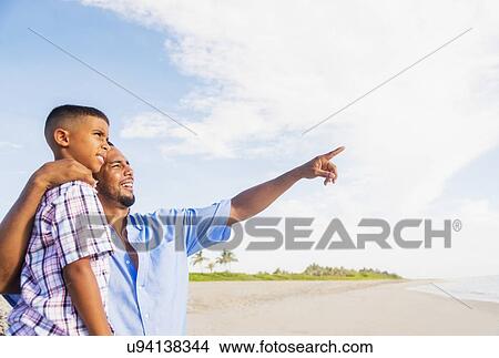 Picture - Father and son (10-11) embracing on beach. Fotosearch