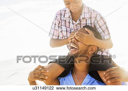 Stock Image - Father and son (10-11) having fun on beach. Fotosearch