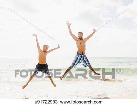 Stock Image - Father and son (10-11) having fun on beach. Fotosearch