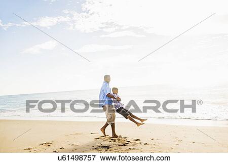 Stock Photo - Father and son (10-11) having fun on beach. Fotosearch