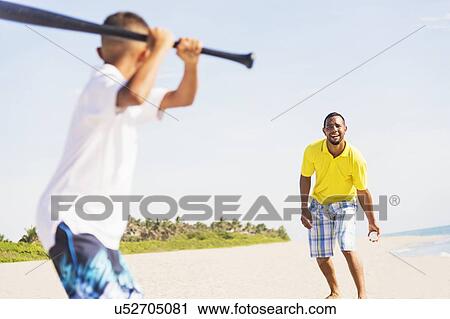 Stock Image - Father and son (10-11) playing baseball on beach. Fotosearch