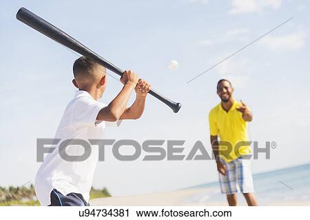 Stock Image - Father and son (10-11) playing baseball on beach. Fotosearch