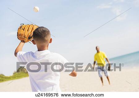 Stock Photograph - Father and son (10-11) playing baseball on beach. Fotosearch