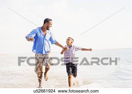 Father and son (10-11) running on beach View Large Photo Image Picture - Father and son (10-11) running on beach. Fotosearch
