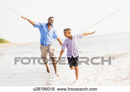 Stock Photo - Father and son (10-11) running on beach. Fotosearch