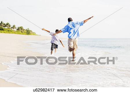 Father and son (10-11) running on beach View Large Photo Image Stock Photo - Father and son (10-11) running on beach. Fotosearch