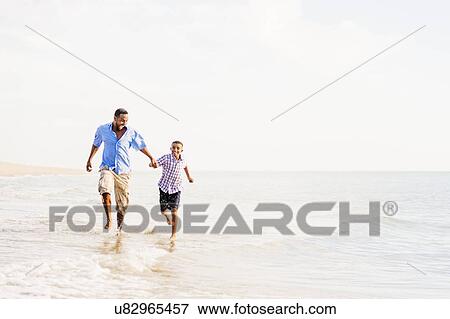 Stock Photo - Father and son (10-11) running on beach. Fotosearch