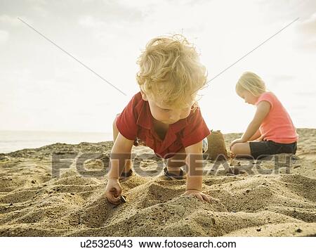 Stock Image - Girl (4-5) and boy (2-3) playing on beach. Fotosearch